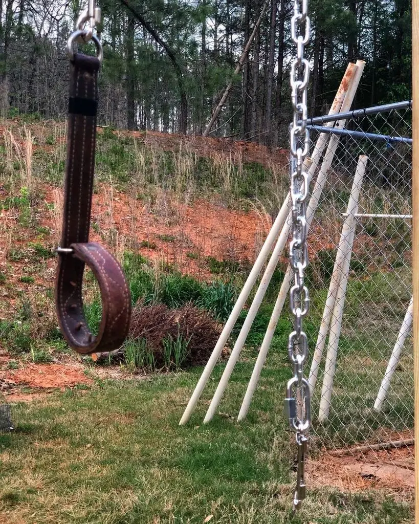 A worn leather collar hanging from the chain by the kennel